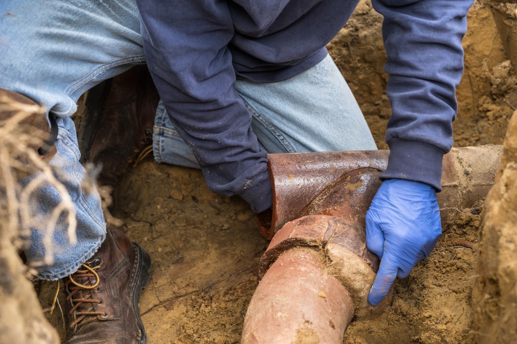 Worker in gloves repairing a broken underground earthenware sewer pipe.