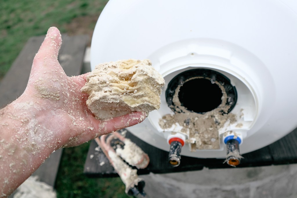 A hand holding a chunk of scale sediment removed from the bottom of a water heater.