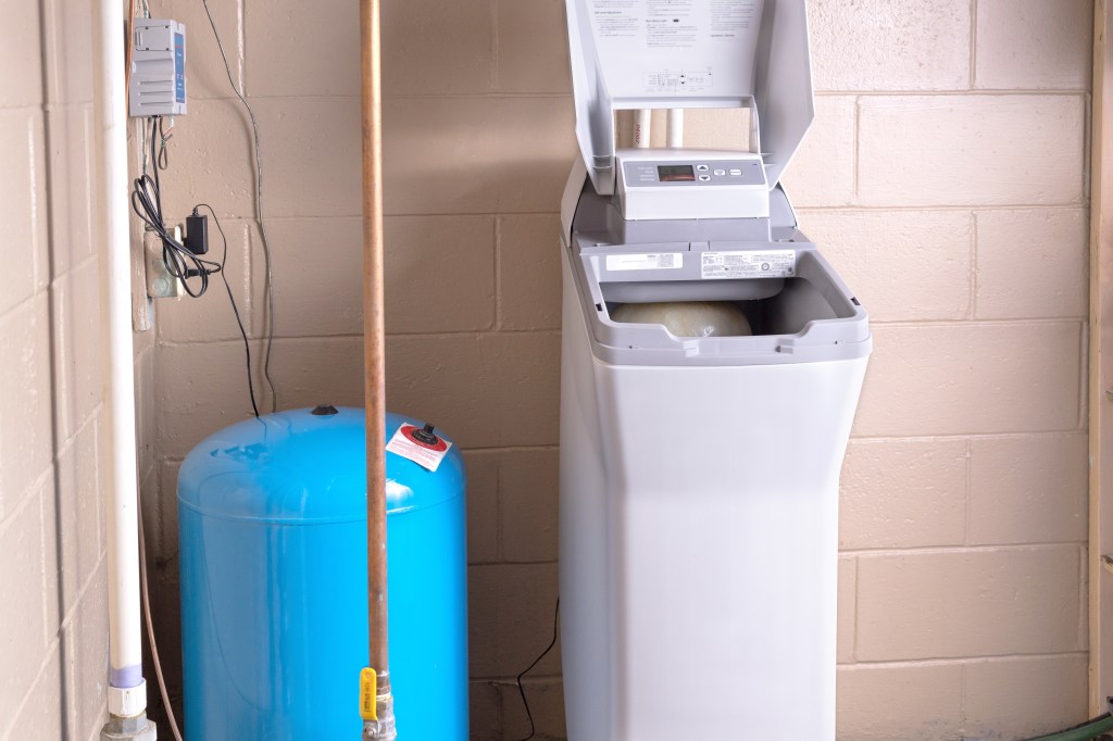 Residential water softener unit next to a blue pressure tank in a utility room.